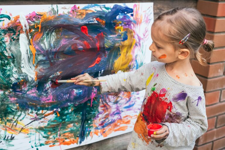 Beautiful little girl painting with various colors on paper, close-up. Art therapy concept