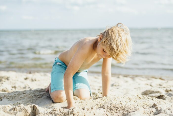 Blond boy playing with sand on the beach